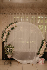 A round white veil screen decorated with flowers is installed in a restaurant during a wedding celebration for a photo shoot with the newlyweds while meeting guests