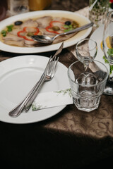 On a table in a restaurant, there is a white plate with cutlery on it and a blank business card to indicate the name of the guest sitting at this place, with various dishes arranged around it
