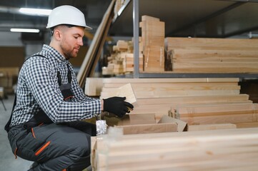 Carpenter picking up wooden plank in furniture factory