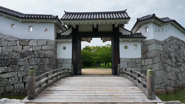 Ako Castle (Japan's Top 100 Castles): A simple wooden arch bridge over the moat connects the wooden gate in towering stone walls, with shooting holes showcasing historical charm.