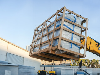 Forklift lifting a wooden crate containing a large, wrapped item outdoors.