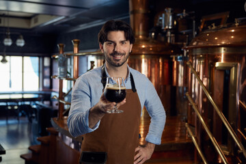 A man brewer wearing an apron and is holding a glass filled with beer