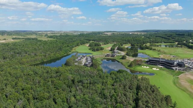 A stunning aerial view of the TPC Toronto golf course in Caledon, Ontario, featuring the modern clubhouse and exclusive luxury residential villas by the water.