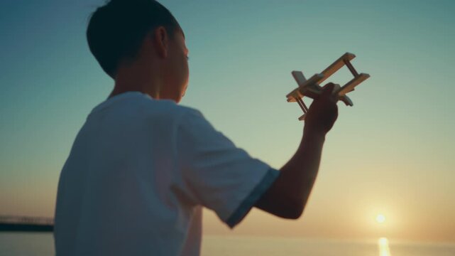 Cinematic slow motion shot with little boy playing with handmade plane model. Happy preteen child resting in nature, summer trip to sea, happy childhood moments, kid exploring world and developing