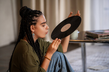 girl with African braids blows dust off a vinyl record.