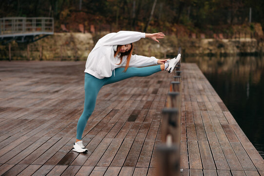 Woman doing fitness exercises on wooden pier near deep lake