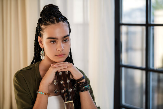 teenage girl with African braids holds a guitar.