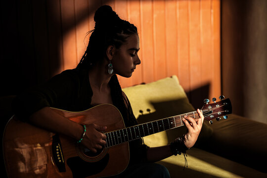 teenage girl playing acoustic guitar in a sunlit room.