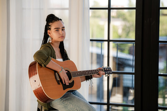 teenage girl playing acoustic guitar in a stylish living room.