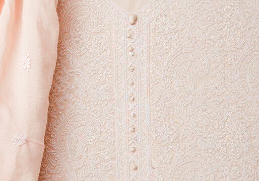 Exquisite Chikankari embroidery in white thread on a pastel peach muslin fabric, showcasing traditional Indian textile art and delicate craftsmanship.