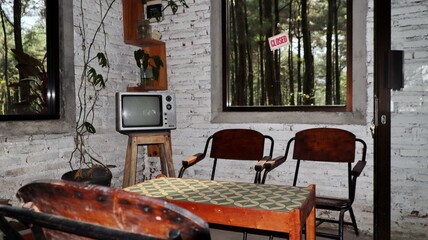 Vintage television sits between two chairs in rustic room with white brick walls, view of forest through window creating cozy atmosphere.