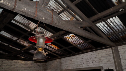 Vintage kerosene lantern hangs from weathered wooden beams in old barn, casting dim light and...