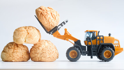 Toy forklift stacks cream puffs like cargo on white; playful bakery scene about making and moving sweets for pastry shop ads and kid‑friendly promos. Photo