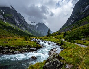 Obraz premium Rushing river winds through a grassy valley beneath looming mountains under a cloudy sky, a path flanking one side
