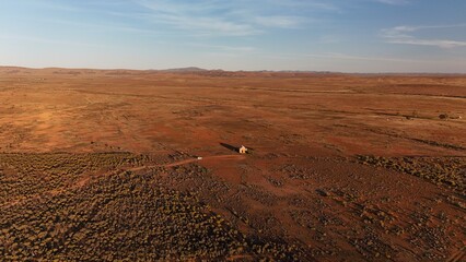 Sunset in the South Australian Outback – Aerial Drone Image of Red Desert Plains, Distant Flinders Ranges, and Isolated Cabin under Golden Evening Light