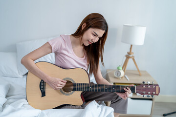 Asian young woman musician playing an acoustic guitar in house.