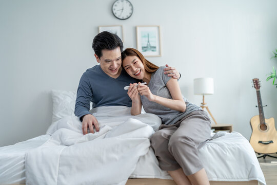 Asian young couple feeling happy after look at positive pregnancy test.