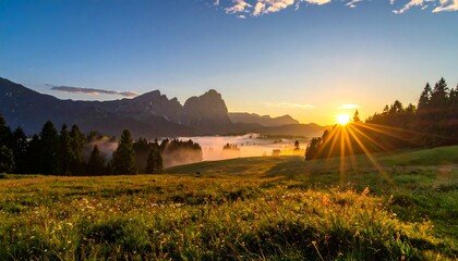 Sunrise over a green field with distant mountains shrouded in mist, trees on the right and blue sky above