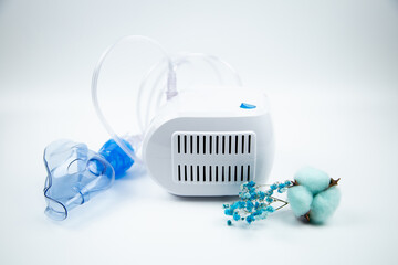 A blue mask for inhalation lies on the side of a white device, surrounded by blue flowers on a...