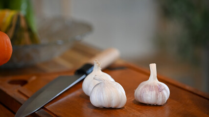 Close up of garlic heads placed on a wooden surface with kitchen knife
