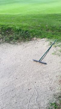 A green golf club is laying on the ground next to a patch of dirt. The dirt is dry and the grass is green