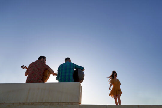 Flamenco guitarists playing music for a dancing woman silhouetted against a bright blue sky