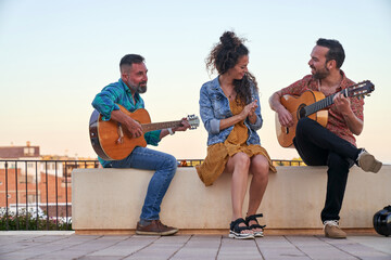 Three people enjoying playing and listening to live flamenco music outdoors. Guitarists performing with a woman clapping