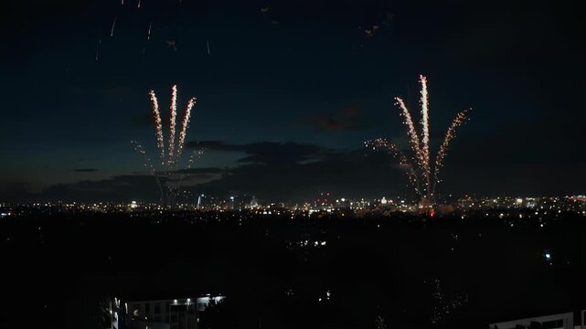 Stunning night scene of firework bursts illuminating a darkened cityscape below. Dramatic flares