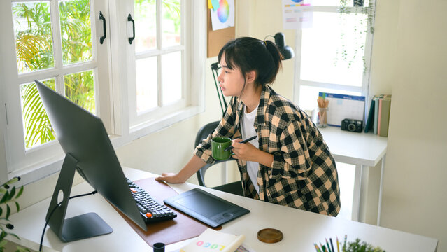 Young graphic designer holding a coffee cup and working in a bright workspace with natural light