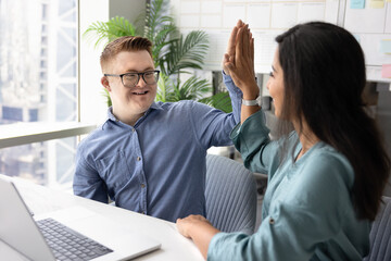 Two happy inclusive company coworkers making high five at workplace