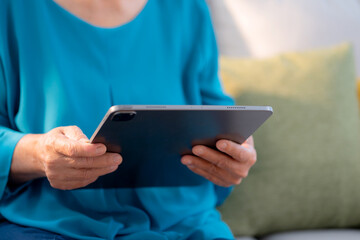 Close up hand senior woman reading tablet in living room at home, online connection and digital...