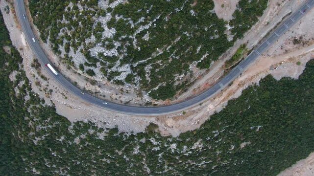 A mountain road making a sharp turn on rugged terrain. Aerial view captured by drone for transportation, travel, logistics, and geography themes. Highway traffic. Drone view for transportation, travel
