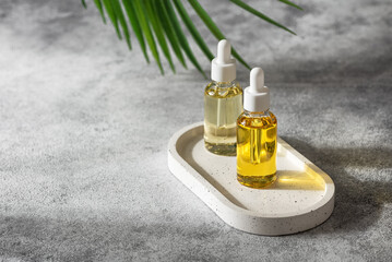 Two dropper bottles with cosmetic serum in sunlight on a gray grunge background with a palm leaf. Selective focus