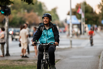 Obraz premium Delivery man riding bicycle in urban street during working hours