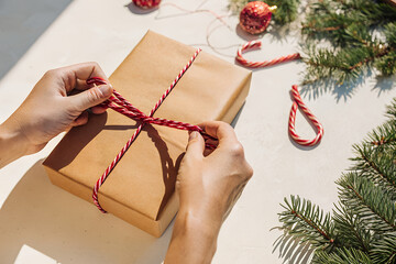 Wrapping a Christmas gift with red ribbon on a wooden table with decorations.
