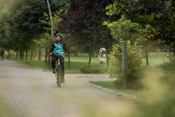 Fototapeta premium Courier riding bicycle in city park delivering food