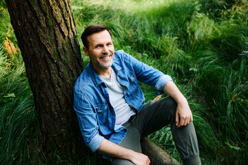 Portrait of smiling man sitting and relaxing in a forest outdoors
