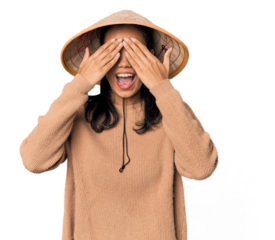 Young Filipina with Vietnamese hat covers eyes with hands, smiles broadly waiting for a surprise.
