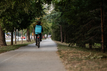 Deliveryman riding bicycle in city park delivering food order