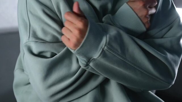 A man is frozen and warms himself by hugging himself with his arms, shivering from the cold.
A young man in a light blue sweater is frozen and warms himself with his hands.