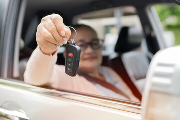 Elderly aged woman showing her new auto key while driving vehicle, sitting at driver seat, smiling to camera