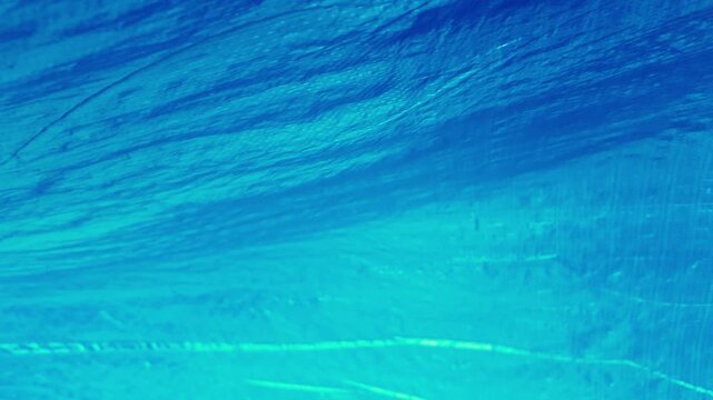 A bright blue textured surface is visible. The lighting highlights the subtle ripples and irregularities in the material. It resembles a close-up of synthetic fabric, plastic sheeting, or tarpaulin.