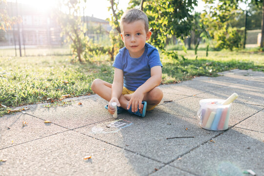 Child drawing with chalk on sidewalk outdoors at playground