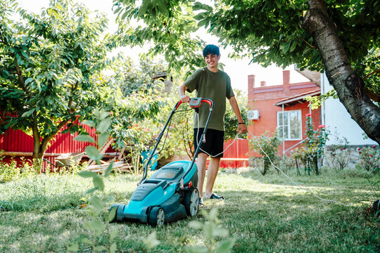 Person mowing lawn with electric lawn mower in backyard garden