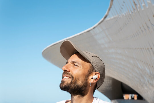 Runner with earbuds stretching outdoors by Maat Lisbon in summer morning