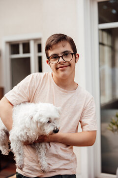 Teenager with trisomy 21 smiling and holding a dog outdoors