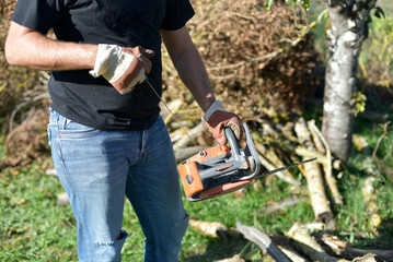 Homme coupant du bois à la tronçonneuse dans le jardin, travail manuel en automne / Man cutting firewood with a chainsaw outdoors in autumn