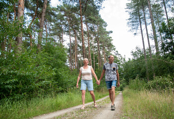 Fototapeta premium Senior couple walking hand in hand along a sunlit forest path, smiling and enjoying peaceful outdoor recreation, companionship and active retirement together