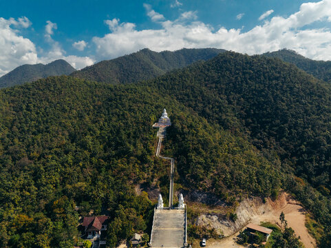 Aerial view of the serene Big Buddha Pai atop a lush mountain, its white form contrasting against the deep greens and blues, Big Buddha Pai, Mae Hi, Thailand.