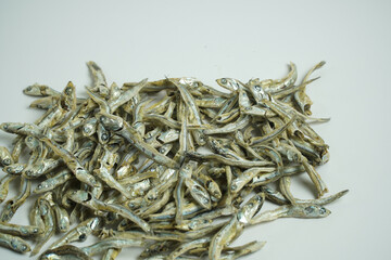 A generous pile of small, silvergrey dried fish, like anchovies or sardines, scattered abundantly on a clean white background.
